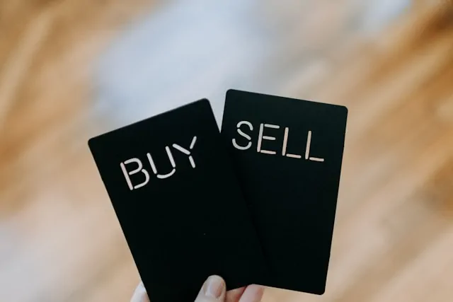 Hands holding 'Buy' and 'Sell' cards