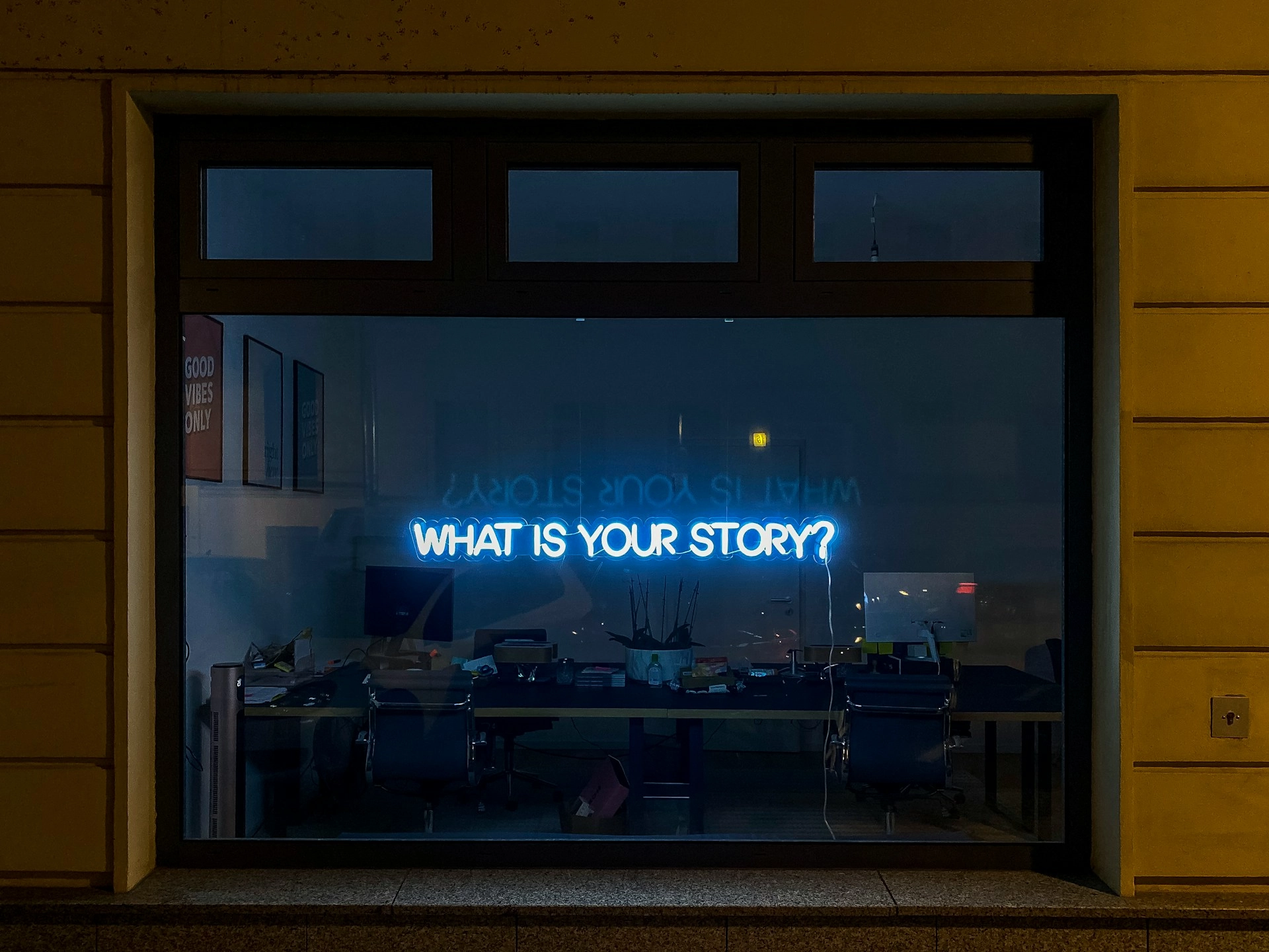 Office window with neon 'What is your story?' sign