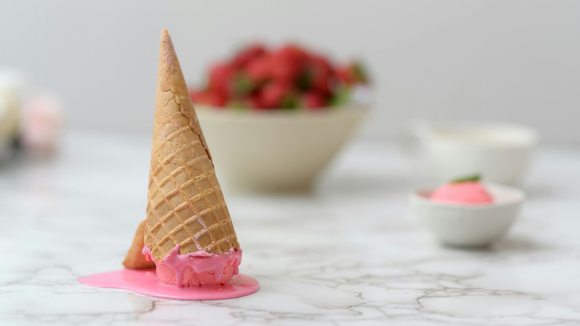 Melting strawberry ice cream cone on marble surface